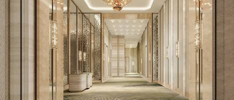 A corridor with a patterned carpet, a chandelier, and mirrored walls.