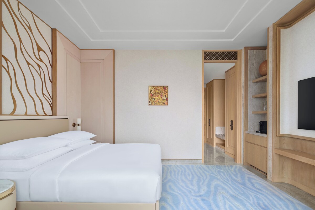 Quarto de hotel com cama, uma obra de arte na parede, um guarda-roupa e televisão.