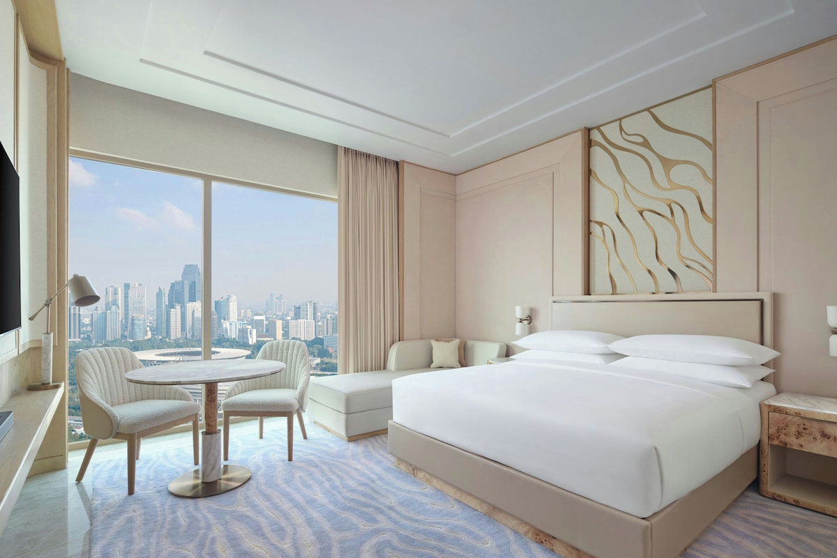 A hotel room with a large bed, a seating area with a table, and a view of a cityscape.