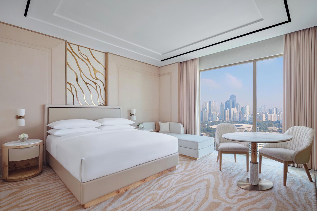 Quarto de hotel com cama grande, área de estar e vista para a cidade.
