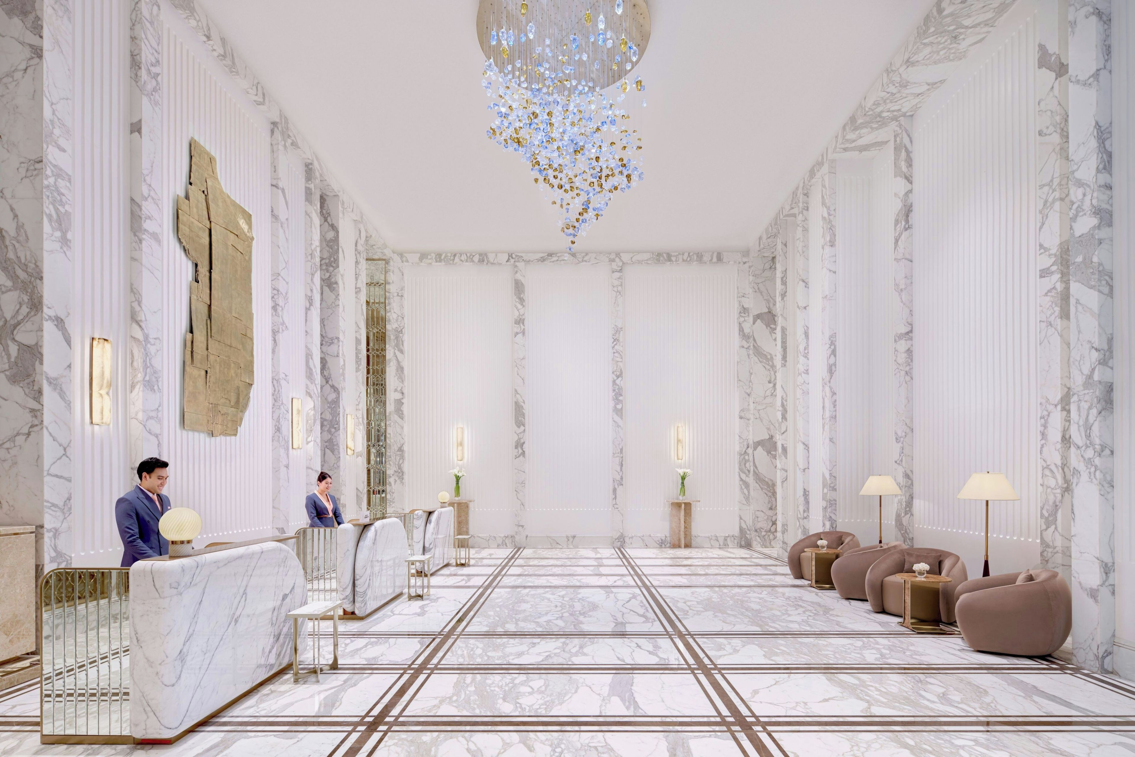 A spacious lobby with marble flooring, a reception desk, seating area, and a chandelier.