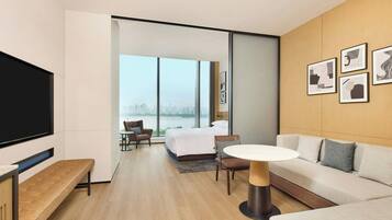 Una habitación de hotel moderna con una cama grande, un sofá, un televisor y un balcón con vista a la ciudad.