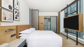 Een moderne hotelkamer met een bed, een bureau, een flatscreen televisie en grote ramen.