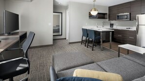 A modern hotel room with a sofa, a dining table with chairs, a kitchen area with a microwave and refrigerator, and a TV. - Residence Inn by Marriott Warner Robins (Warner Robins)