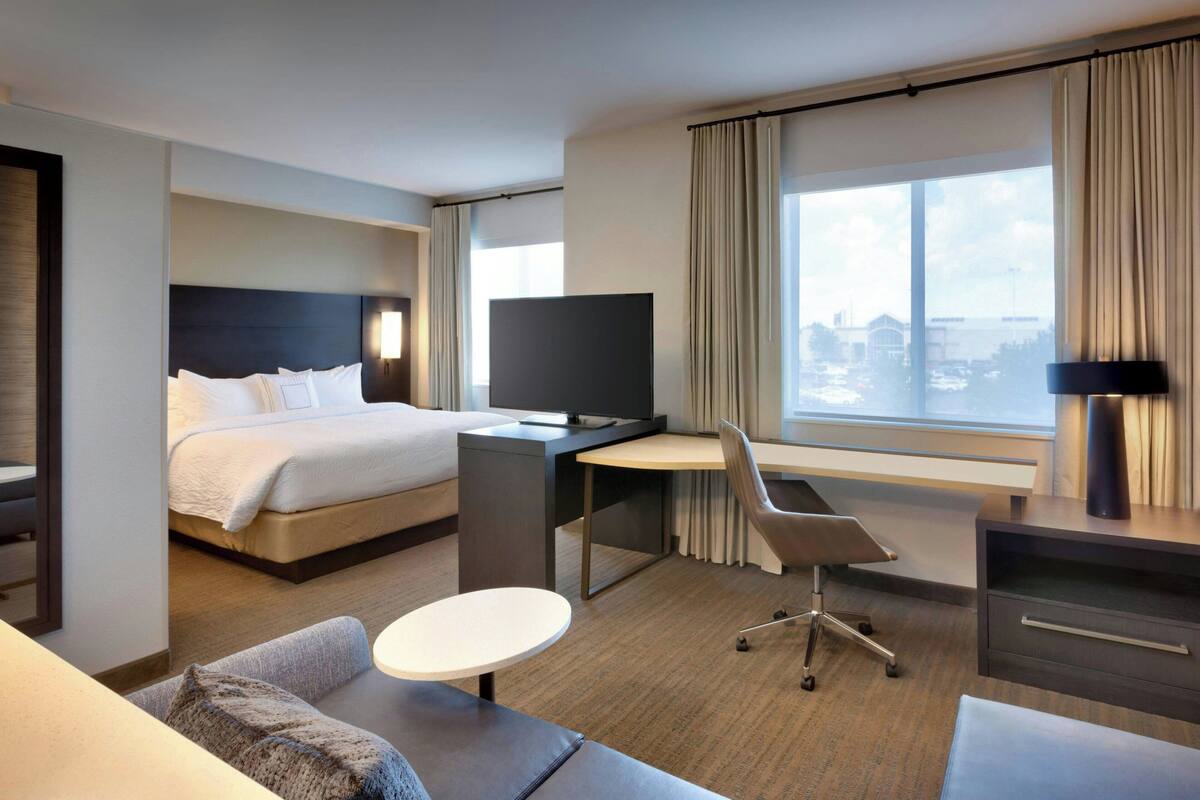 A hotel room with a bed, desk, chair, and a large window with a view.