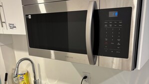 A kitchen with a stainless steel microwave, a toaster, a kettle, and a sink with a dish rack. - Victorious Place(STRA-2025-2882840) (Winnipeg)