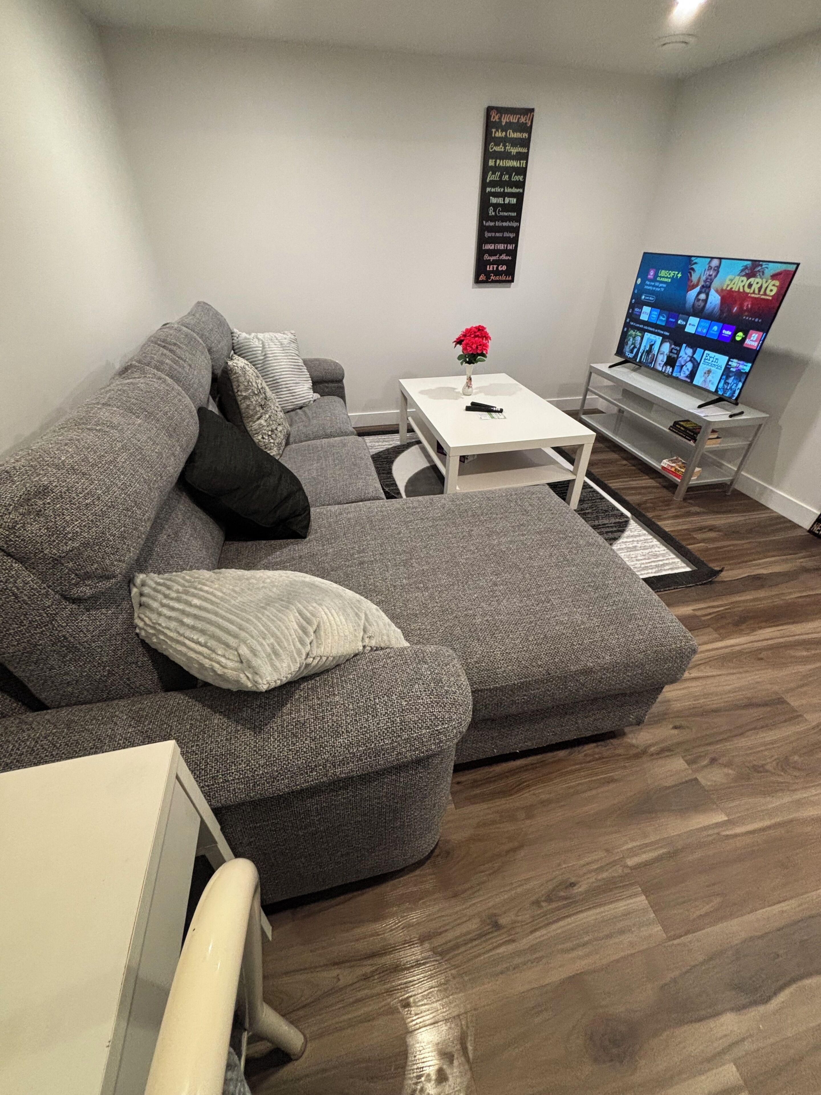 Een moderne woonkamer met een grijze modulaire bank, een witte salontafel, een flatscreen televisie en een bord aan de muur.