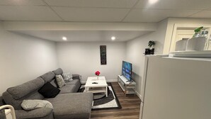 A modern living room with a grey sectional sofa, a white coffee table, a flat-screen TV, and a refrigerator. - Victorious Place(STRA-2025-2882840) (Winnipeg)