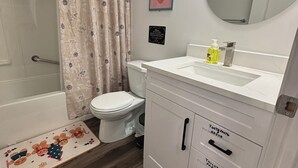 A bathroom with a toilet, a shower curtain, a sink with a mirror, and a cabinet with labeled drawers. - Victorious Place(STRA-2025-2882840) (Winnipeg)