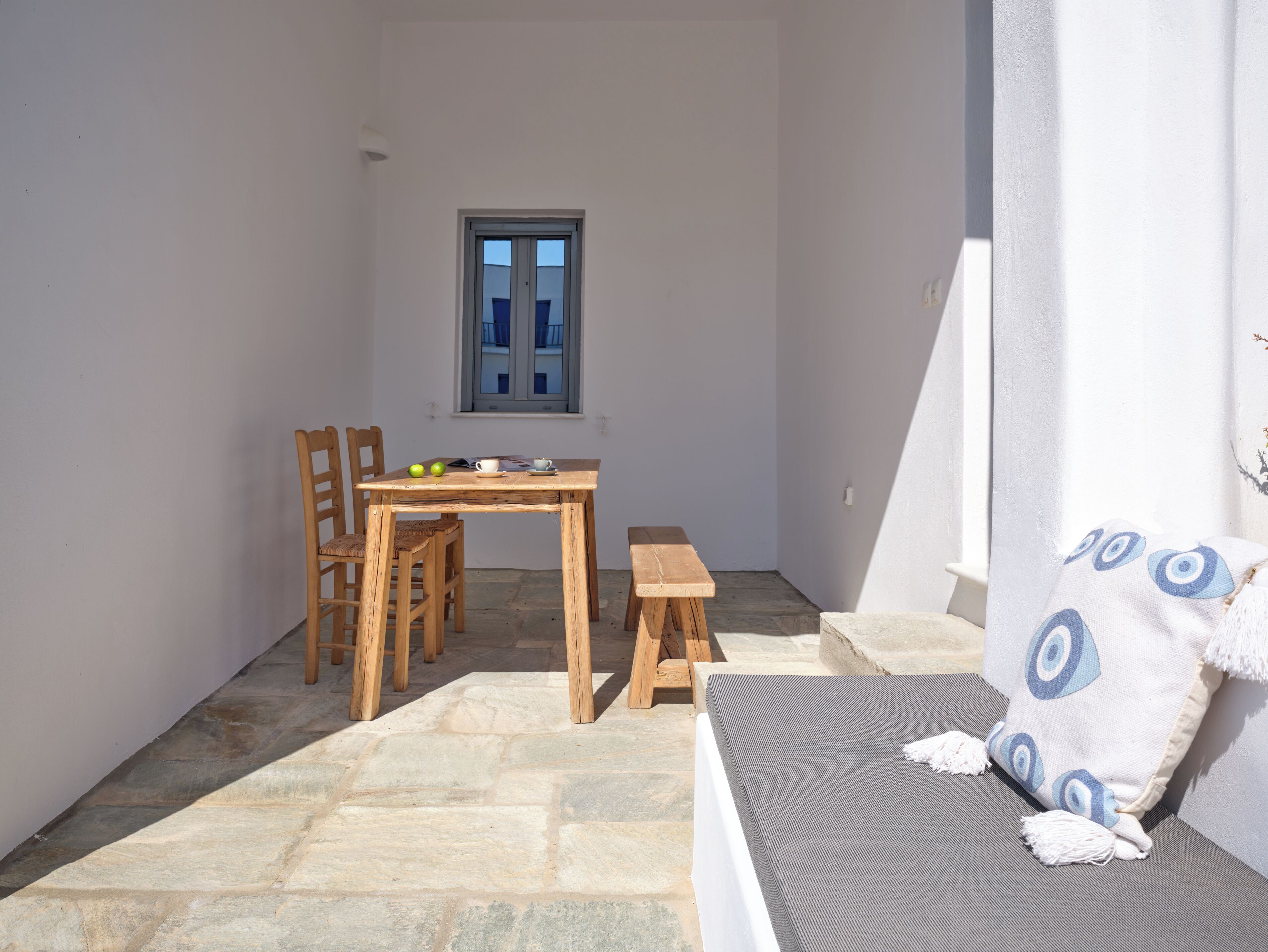 A small, sunlit room with a wooden table, chairs, a bench, and a window.