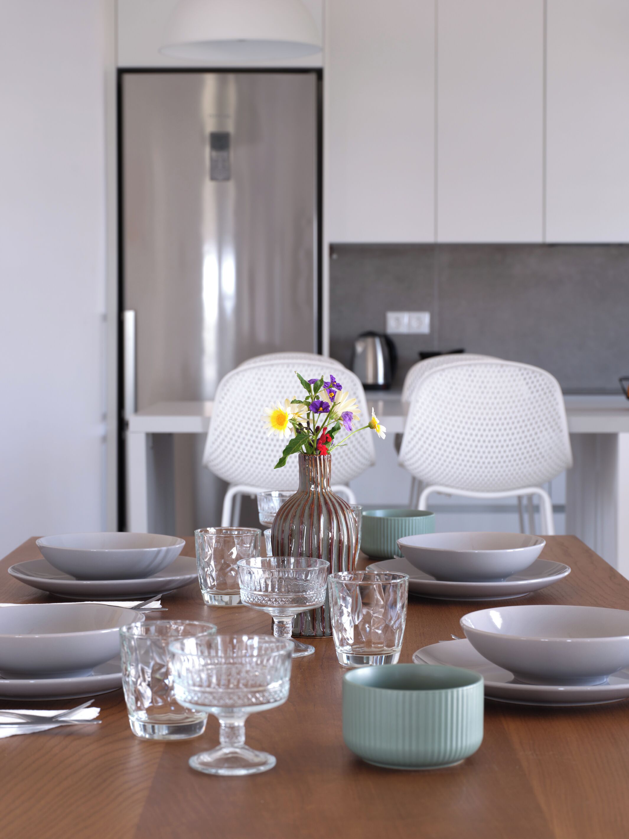 Una mesa de comedor dispuesta con platos, tazones y vasos, con un florero en el centro.