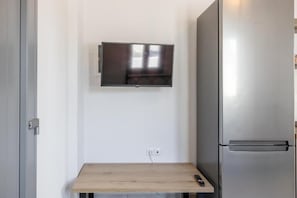 A small kitchenette with a built-in TV, a stainless steel refrigerator, and a wooden table. - Mouragio Stay (Aliki)