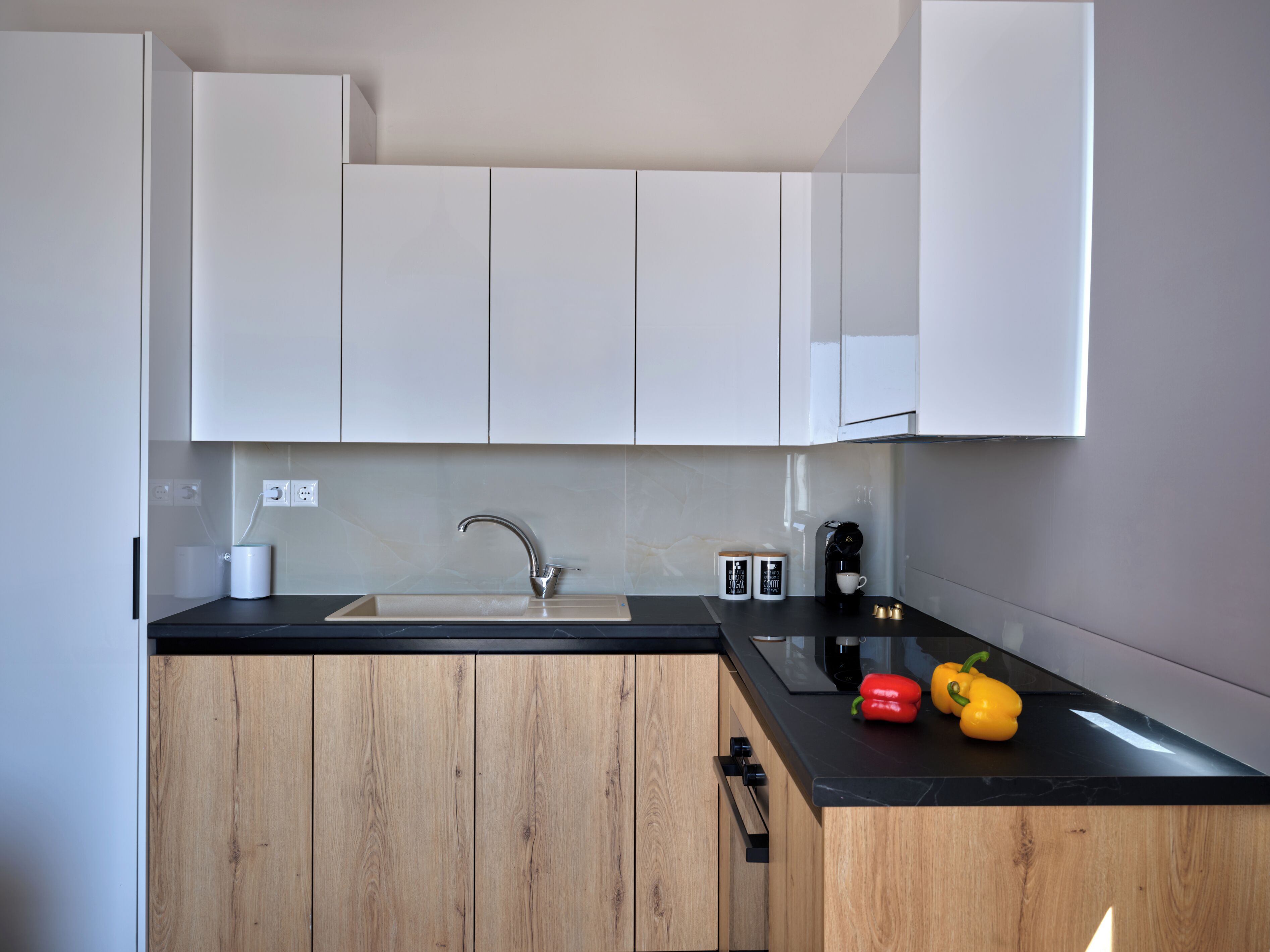 Una cocina moderna con encimera negra, armarios de madera, un lavamanos de acero inoxidable y una cafetera.