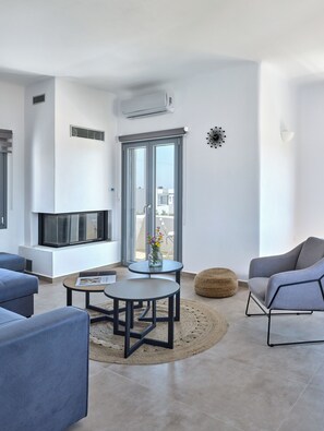 A modern living room with a fireplace, a large window, and a view of the city. - Mouragio Stay (Aliki)
