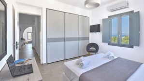 Een slaapkamer met een bed, een bureau met een laptop, een stoel, een kledingkast, een televisie en een raam met uitzicht.
