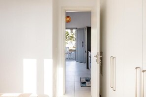 A hallway with a door leading to a kitchen area, a hanging light fixture, and a view of the outside. - Mouragio Stay (Aliki)