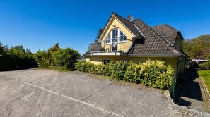 En gul byggnad med en balkong, en asfalterad uppfart och en satellantenn.