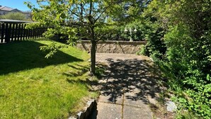 A stone pathway leading through a garden with a tree and a stone wall on one side. - Haus Seeblick - Comfort Apartment No. 2 with lake view (Binz)