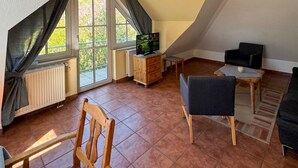 Un soggiorno spazioso con soffitto a falde, una televisione su un mobile in legno, un divano, una poltrona e un tavolino.
