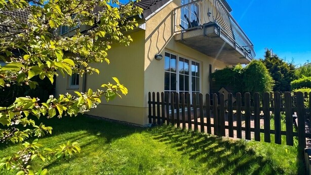 Una casa a due piani con un balcone, un recinto in legno a paletti e un prato curato.