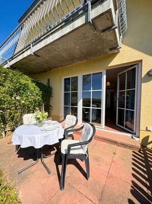 An outdoor patio with a table set for dining, chairs, and a balustrade above. - Haus Seeblick - Comfort Apartment No. 1 with lake view (Binz)