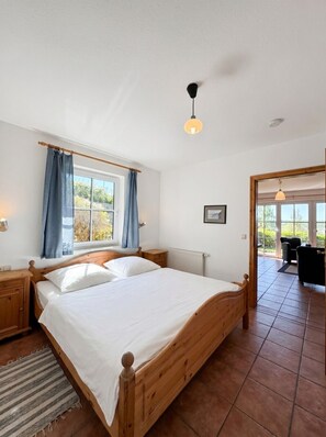 A bedroom with a wooden bed, a window with curtains, a radiator, and a view of the outdoors. - Haus Seeblick - Comfort Apartment No. 1 with lake view (Binz)