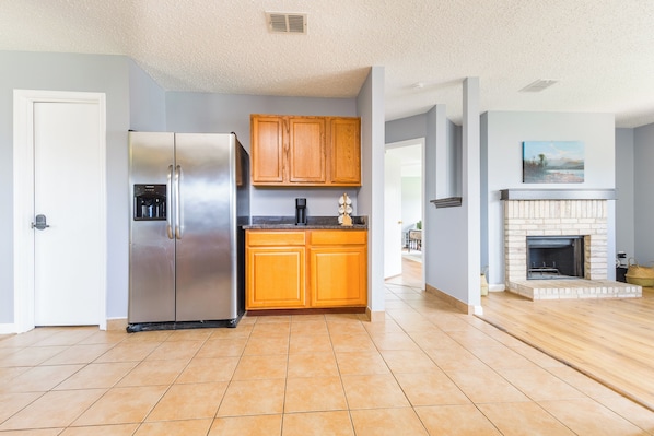 A kitchen with a stainless steel refrigerator, wooden cabinets, and a fireplace.