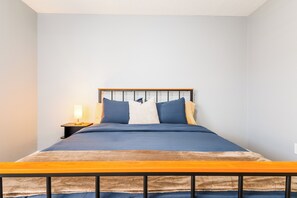 Ein Bett mit Holz-Kopfteil, ein Nachttisch mit Lampe und eine Wandsteckdose.
