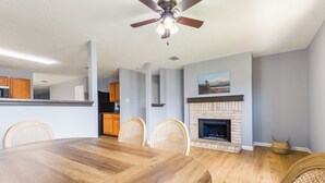 Ein Essbereich mit Holztisch, Korbstühlen, Deckenventilator und Kamin.