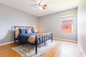 Ein Schlafzimmer mit einem Bett, einem Deckenventilator, einem Fenster mit Jalousien und einem gemusterten Teppich.
