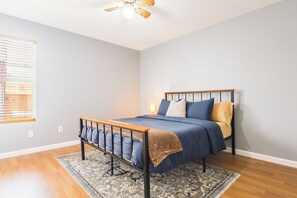 Ein Schlafzimmer mit einem Bett, einem Deckenventilator, einem Fenster mit Jalousien und einem gemusterten Teppich.