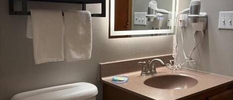 A bathroom with a toilet, sink, mirror, towel rack, and hairdryer.