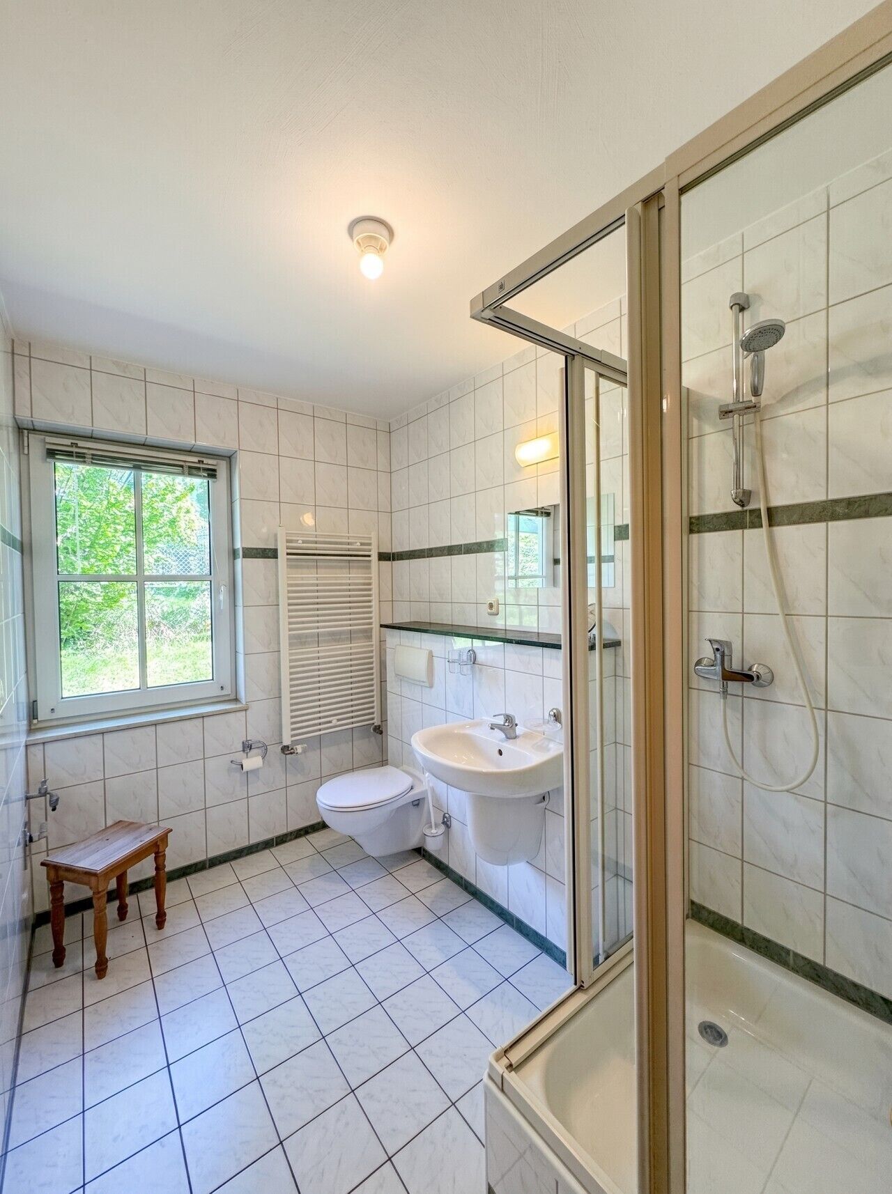 A bathroom with a toilet, sink, shower, and a small wooden stool.