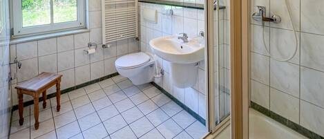A bathroom with a toilet, sink, shower, and a small wooden stool.