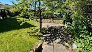 A stone pathway leading through a garden with a tree and a stone wall on one side. - House Seeblick - Garden Suite No. 4 (Binz)