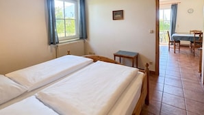 A room with two single beds, a small table, a chair, a window with curtains, and a view of an outdoor area. - House Seeblick - Garden Suite No. 4 (Binz)