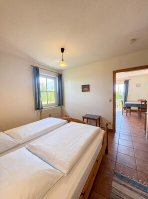 A room with two single beds, a small table, a chair, a window with curtains, and a view of an outdoor area. - House Seeblick - Garden Suite No. 4 (Binz)