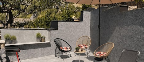 An outdoor patio with two wicker chairs, a table, and a large umbrella.