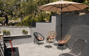 Eine Terrasse im Freien mit zwei Korbstühlen, einem Tisch und einem großen Sonnenschirm.