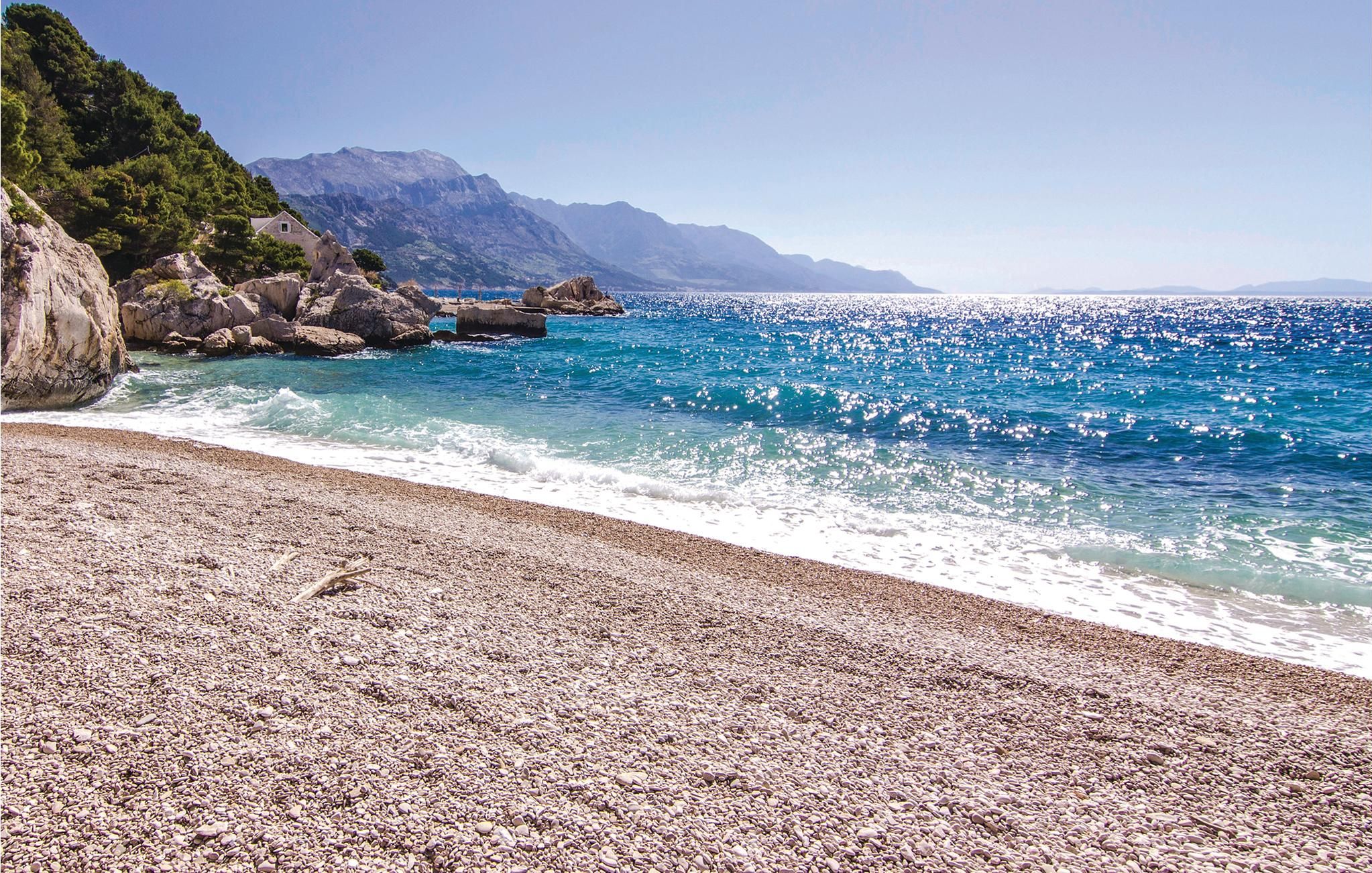 Une plage de galets bordée d’une eau d’un bleu limpide, avec des montagnes en toile de fond.