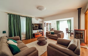 Ein Wohnzimmer mit Sofa, Sesseln, Fernseher, Kamin und einer Holzkommode.