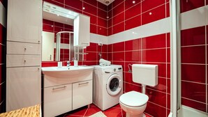 Ein kleines Badezimmer mit Waschbecken, Spiegel, Waschmaschine, Toilette und einem Schrank.