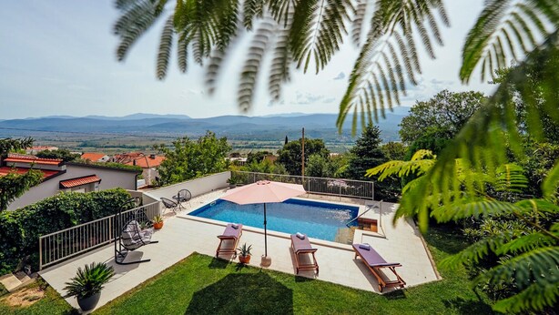 Una piscina amb gandules, envoltada de vegetació i vista a muntanyes allunyades.