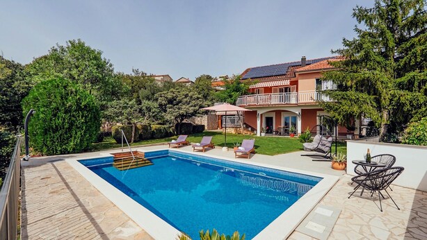 Ein rechteckiger Pool mit Holzterrasse, umgeben von einem gepflegten Rasen und Bäumen.
