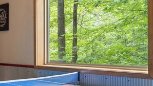 A ping pong table with paddles and a ball, a window with a view of a forest, and a wall with a sign. - Peaceful 4-bedroom cabin with AC in charming Cosby (Cosby)