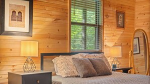 A wooden-paneled bedroom with a bed, bedside lamps, a nightstand, and a mirror. - Peaceful 4-bedroom cabin with AC in charming Cosby (Cosby)