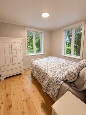 Ein Schlafzimmer mit einem Bett, zwei Fenstern, einem Kleiderschrank und einer Deckenleuchte.
