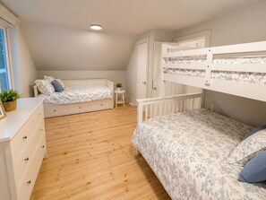 Ein Schlafzimmer mit einem Etagenbett, einem Einzelbett, einem Schminktisch, einem kleinen Tisch und einer Topfpflanze.