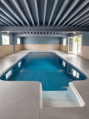Ein großer, überdachter Pool mit gerader und geschwungener Seite, umgeben von Wänden mit Fenstern und einer Tür.