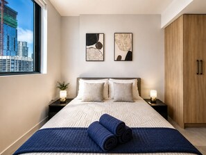 Ein modernes Hotelzimmer mit einem großen Bett, zwei Wandbildern, Blick auf die Stadt durch ein Fenster und einem Holzschrank.